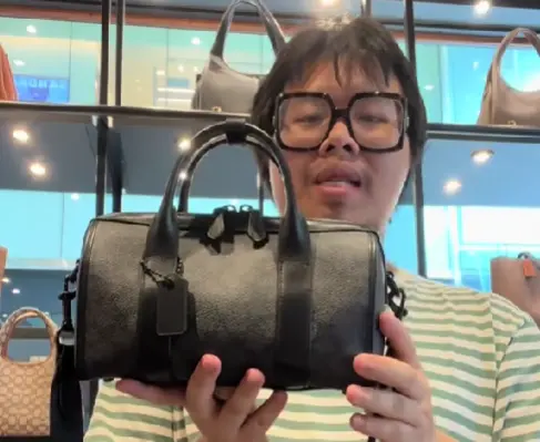 Brandon Nguyen showcasing a small black duffle bag from Coach.